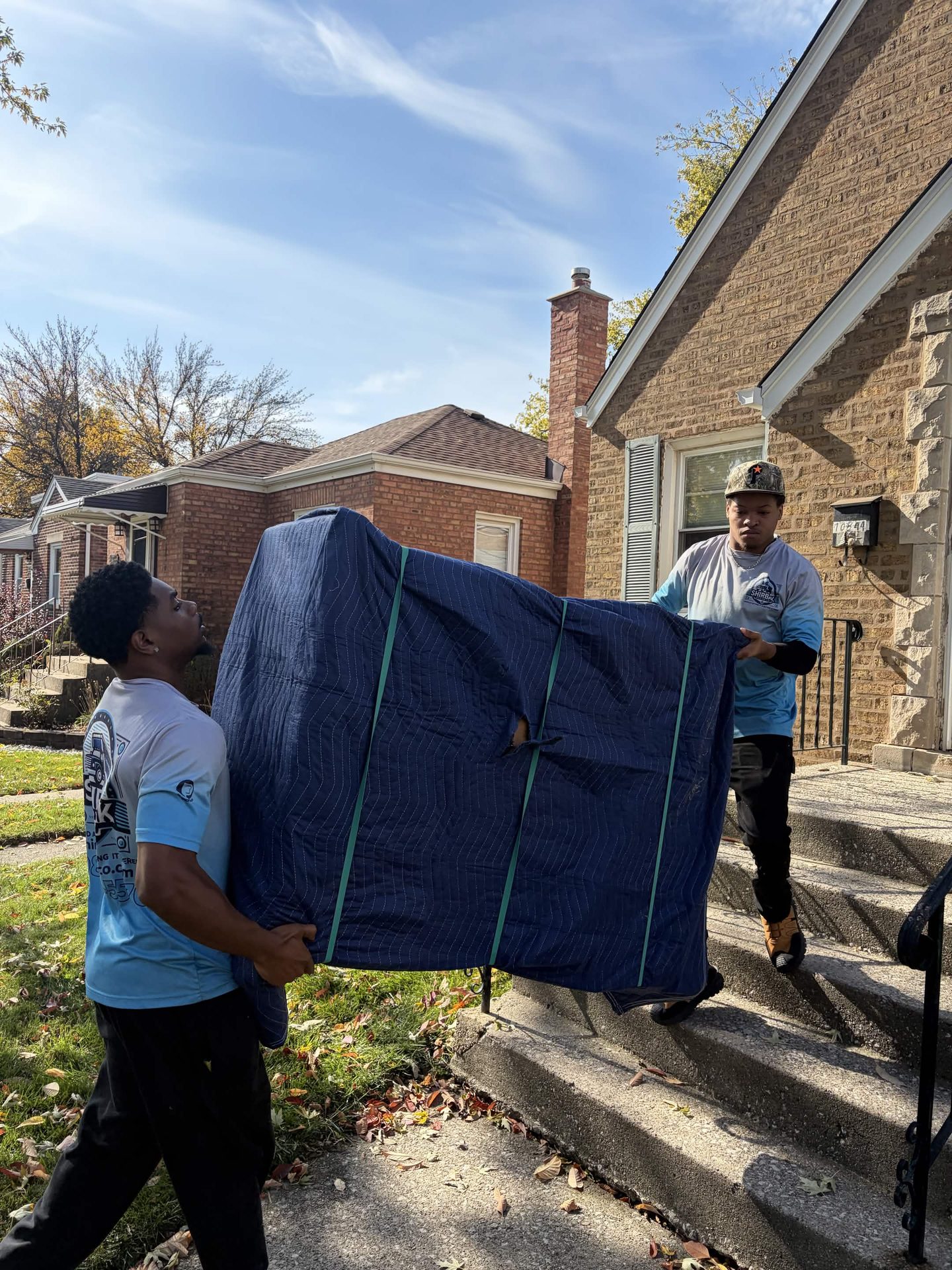 ShirBak movers carry blanket-wrapped furniture down outdoor steps.